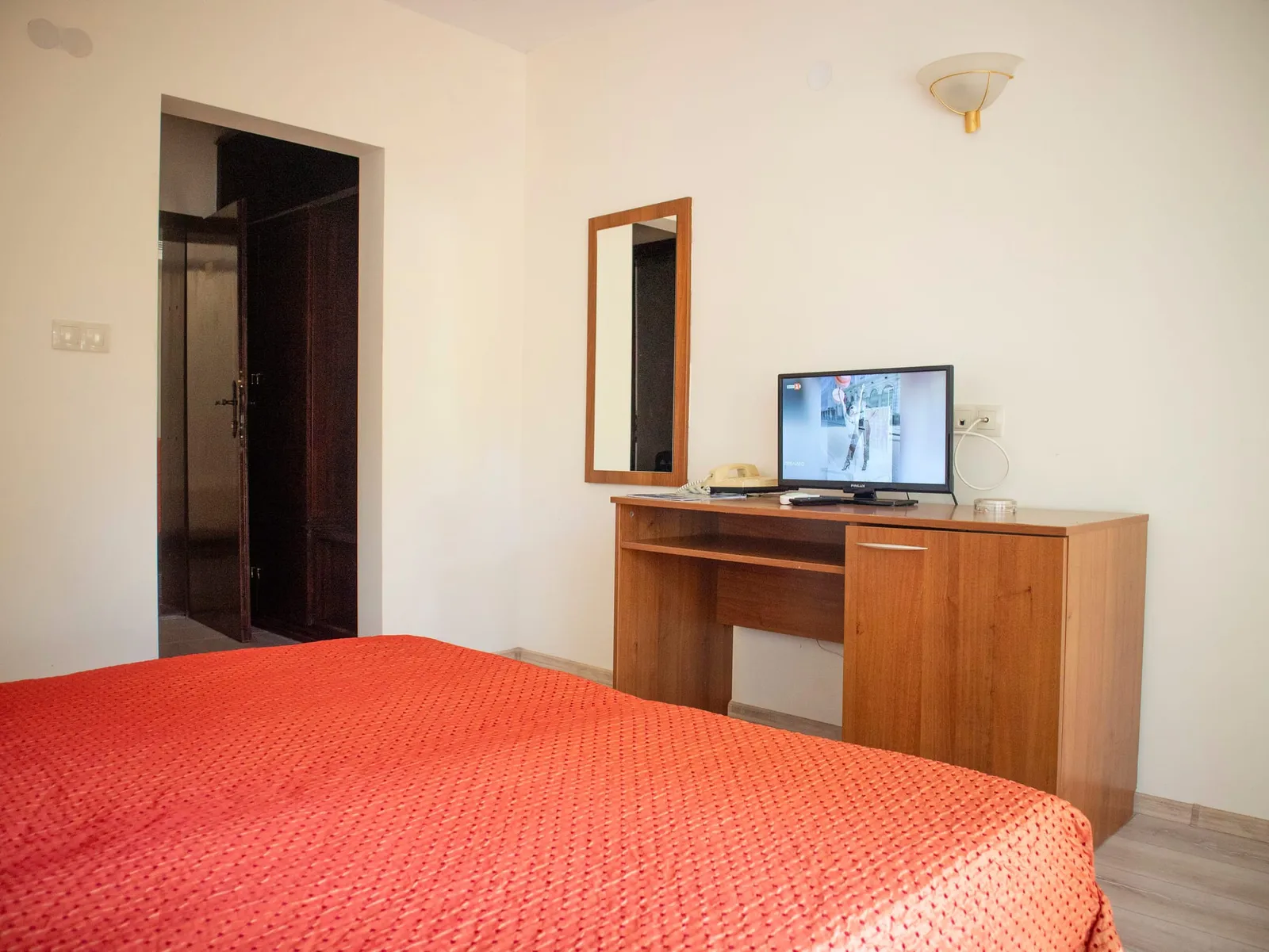 Einzelzimmer: Bett, Schreibtisch mit Fernseher und Zimmereingang
