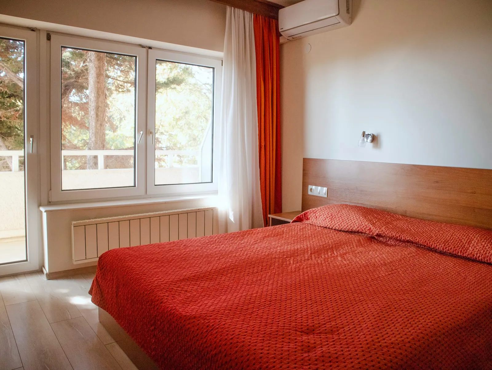 Einzelzimmer: Bett mit Holzkopfteil neben einem Fenster zu den Bäumen